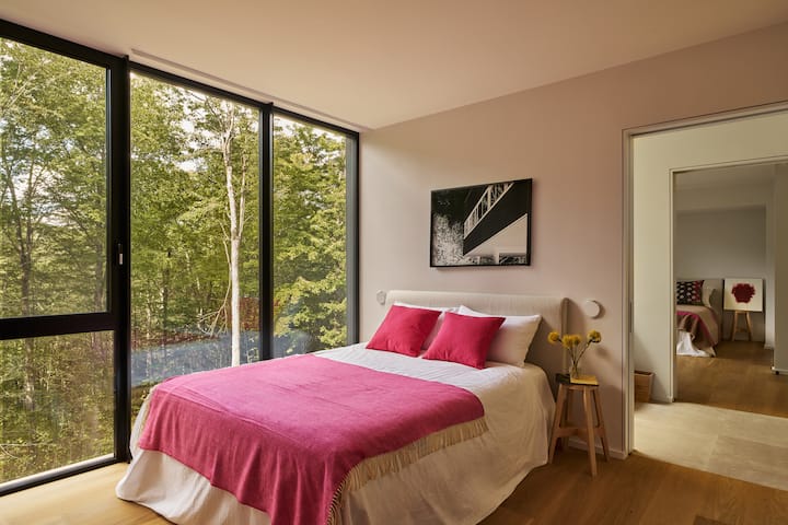 Dormitorio de invitados con cama tamaño queen en la planta superior con un gran armario, ventanas de suelo a techo con un baño Jack and Jill entre este dormitorio y otro dormitorio con cama tamaño queen.