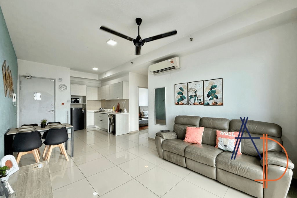 A modern living area showcases a comfortable leather sofa with colorful cushions. A dining table for four is positioned nearby, with the kitchen in the background equipped with essential appliances. Light-colored walls and large windows enhance the spacious feel of the room.