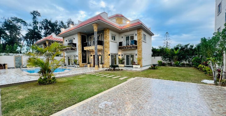 A spacious outdoor area is presented, featuring an inviting pool among manicured grass and landscaped plants. The two-story house showcases a blend of modern architecture and natural elements, with large windows and balconies that overlook the garden.