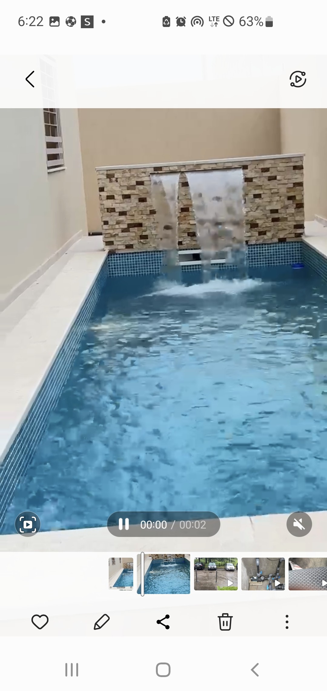 A serene swimming pool features clear blue water, enhanced by a decorative stone water wall. The surrounding area is designed for privacy, with light-colored tiles and smooth edges creating a calm atmosphere for relaxation.