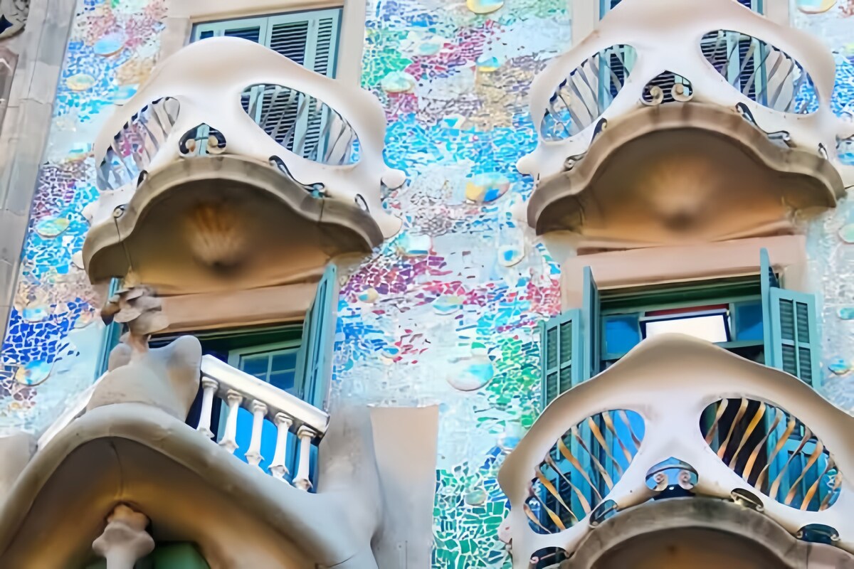 The facade of a modernist building features wavy, sculptural shapes and colorful mosaic tiles. Large balconies with elaborate railings and green shutters create a unique architectural design, reflecting the creativity of Barcelona's artistic heritage.