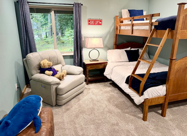 Un espacio lúdico y práctico con una litera doble, un cómodo sillón reclinable, un armario y una zona de juegos infantiles con bloques y una mesa de su tamaño.