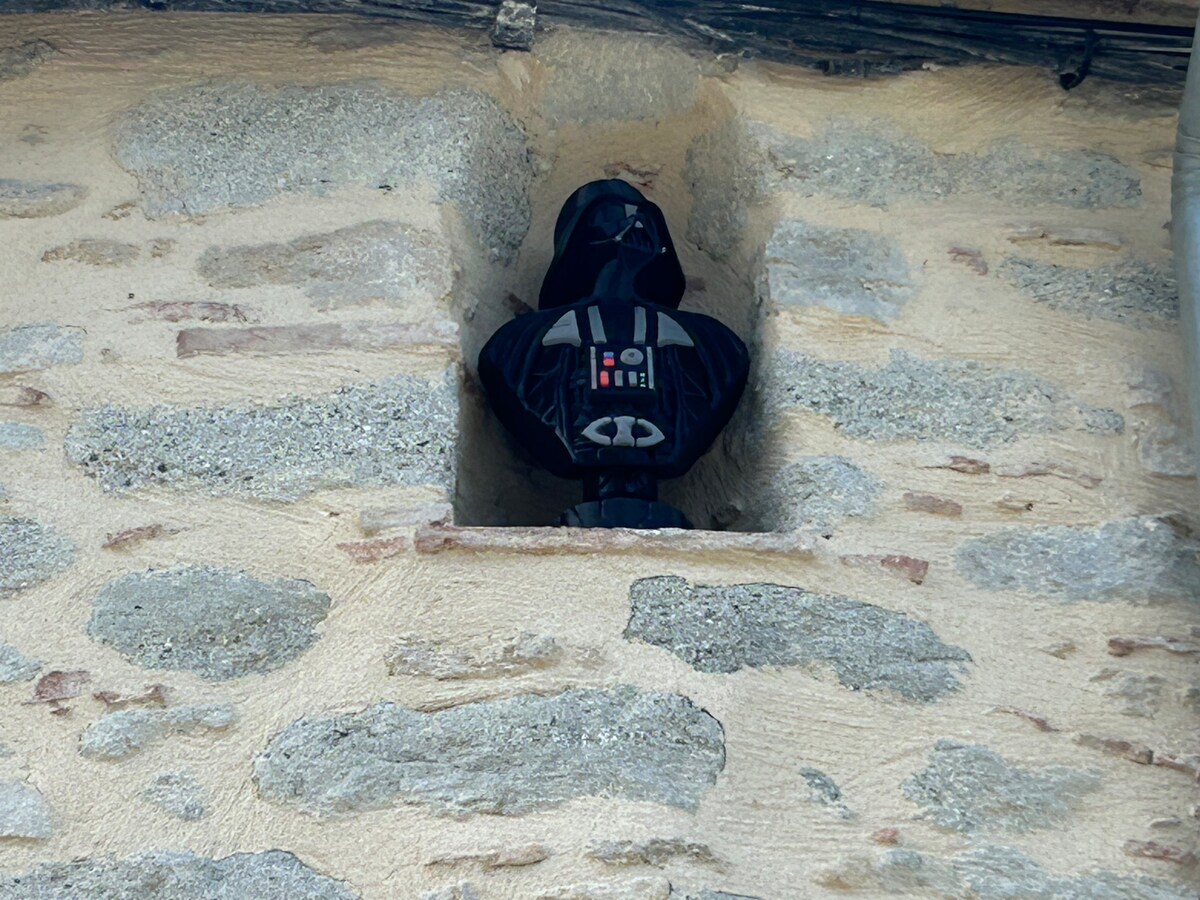 A decorative figure resembling a character from a popular sci-fi franchise is positioned within a stone alcove. The figure is dressed in black and features a distinct emblem on its chest, offering a playful accent to the rustic stone wall.