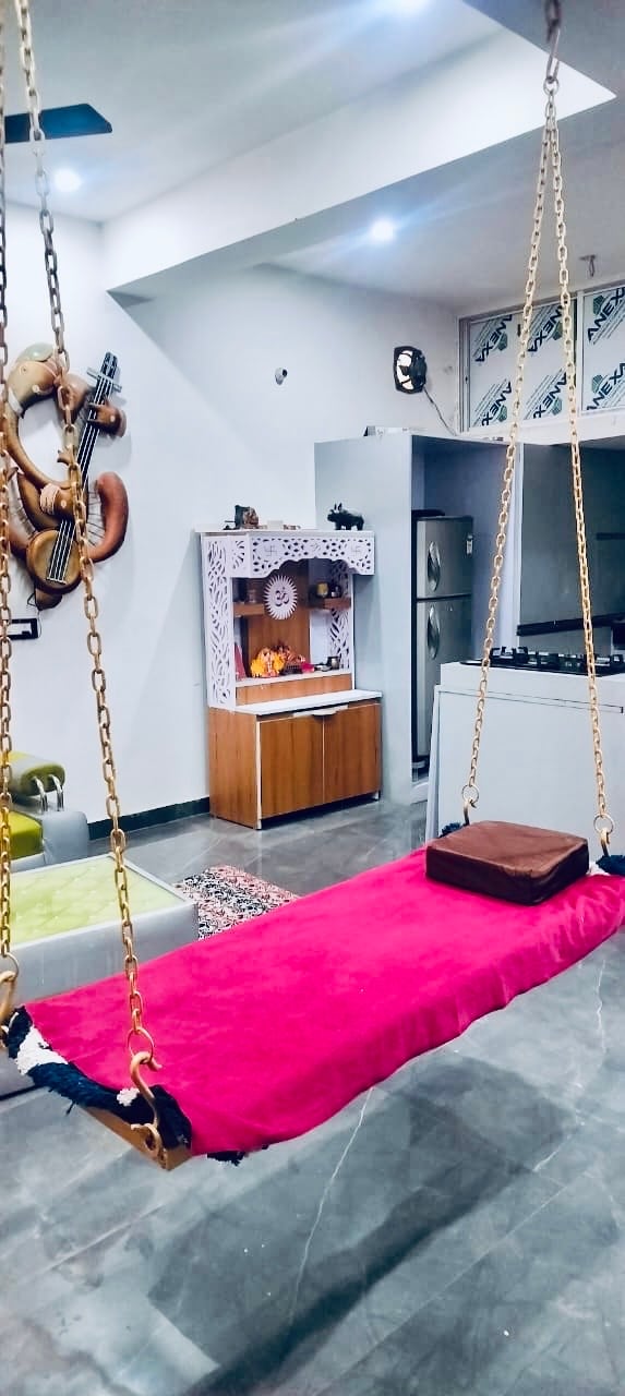 A vibrant pink swing hangs from the ceiling, offering a playful relaxation spot. Surrounding elements include a wooden display cabinet, a refrigerator, and a glimpse of kitchen appliances, all situated in a modern open-concept area with polished flooring.