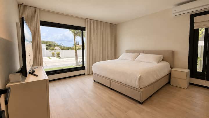 Uma vista iluminada do segundo quarto king mostra seu amplo espaço e luz natural, ao mesmo tempo em que oferece ar condicionado, cortinas para escurecer o quarto, dois guarda-roupas espaçosos e um banheiro privativo.