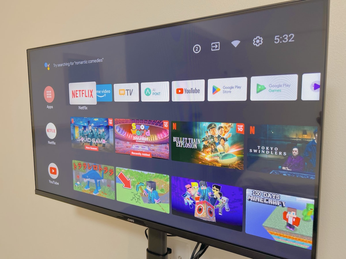 A flat-screen television displays a user interface featuring popular streaming apps such as Netflix, YouTube, and TV. Various titles are highlighted, including a game-themed interface with vibrant images. The device is positioned on a stand, providing comfortable viewing access.