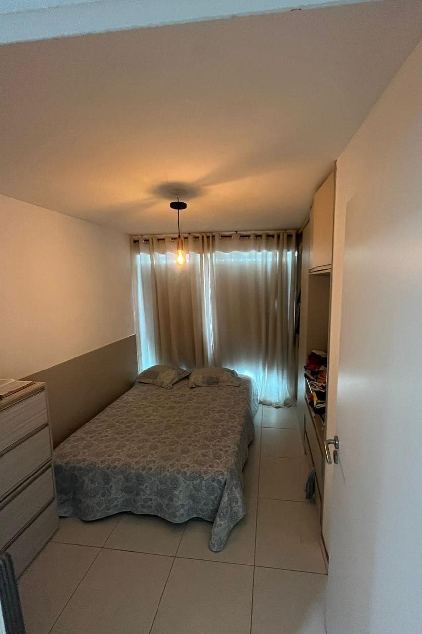 A cozy bedroom is presented with a spacious bed covered in a patterned blanket. Natural light filters through sheer curtains, providing soft illumination. A compact dresser occupies one side, while a closet offers additional storage options.