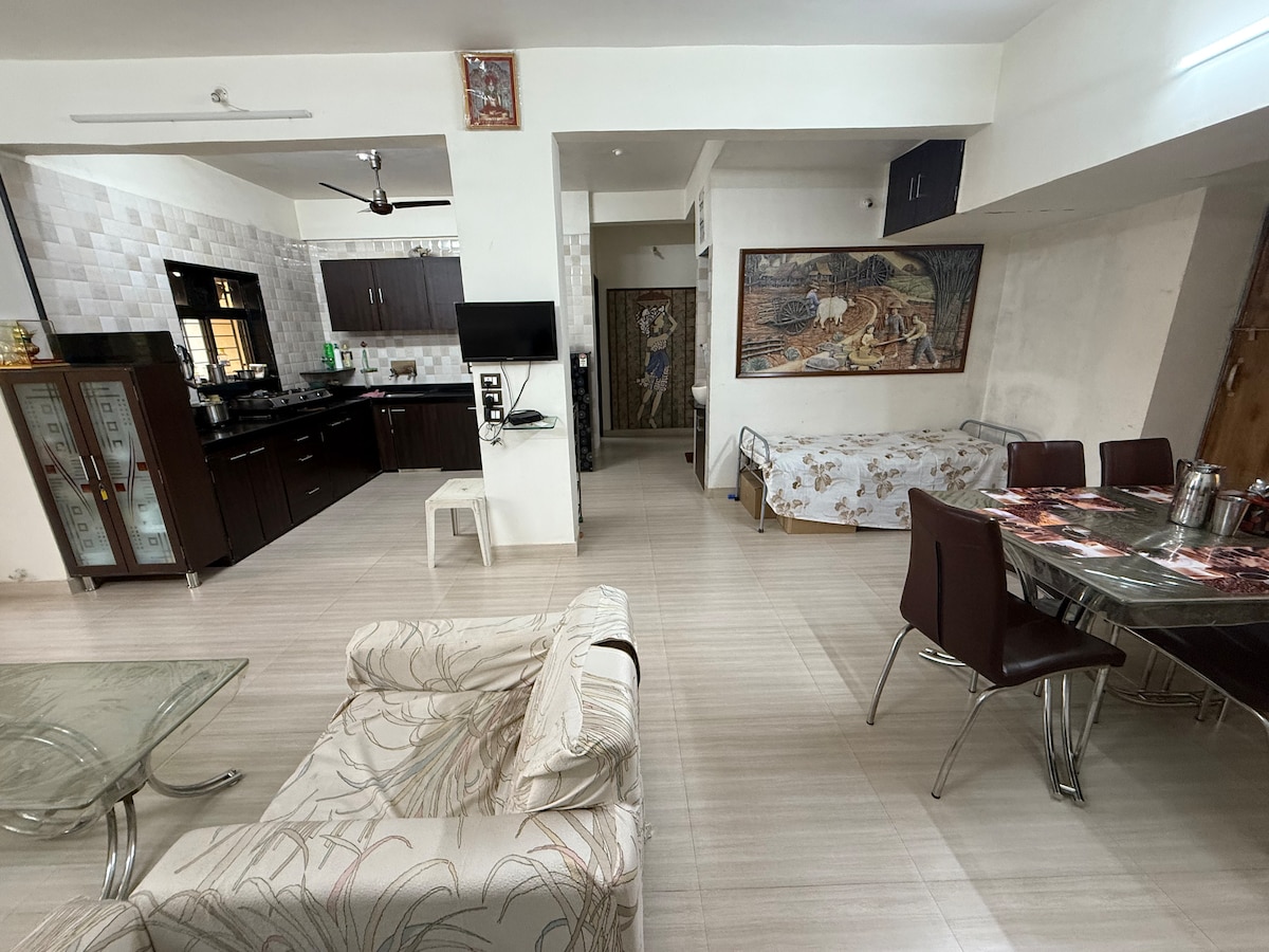 An open-plan living area is visible, featuring a kitchen with dark cabinets and a dining space with a glass table. A comfortable sofa with light upholstery complements the space. Natural light enters through windows, enhancing the simplicity of the decor.