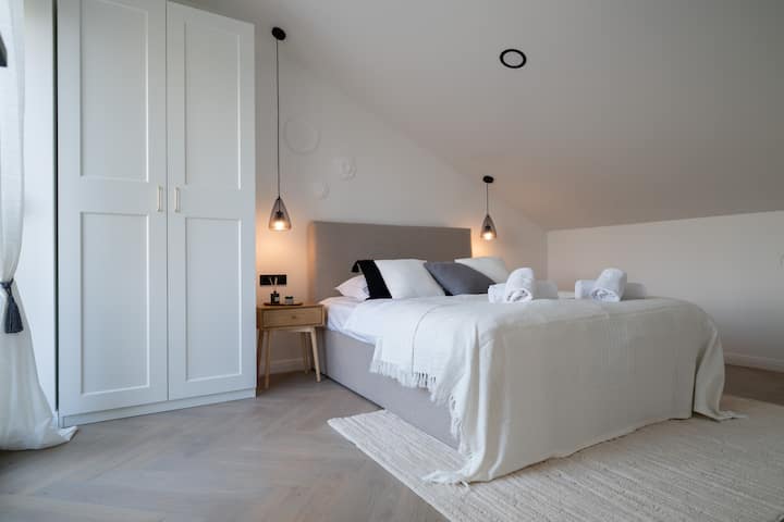 Elegant soveværelse med en behagelig dobbeltseng og direkte adgang til en privat tagterrasse med jacuzzi, liggestole og panoramaudsigt – din egen private spa-oase.