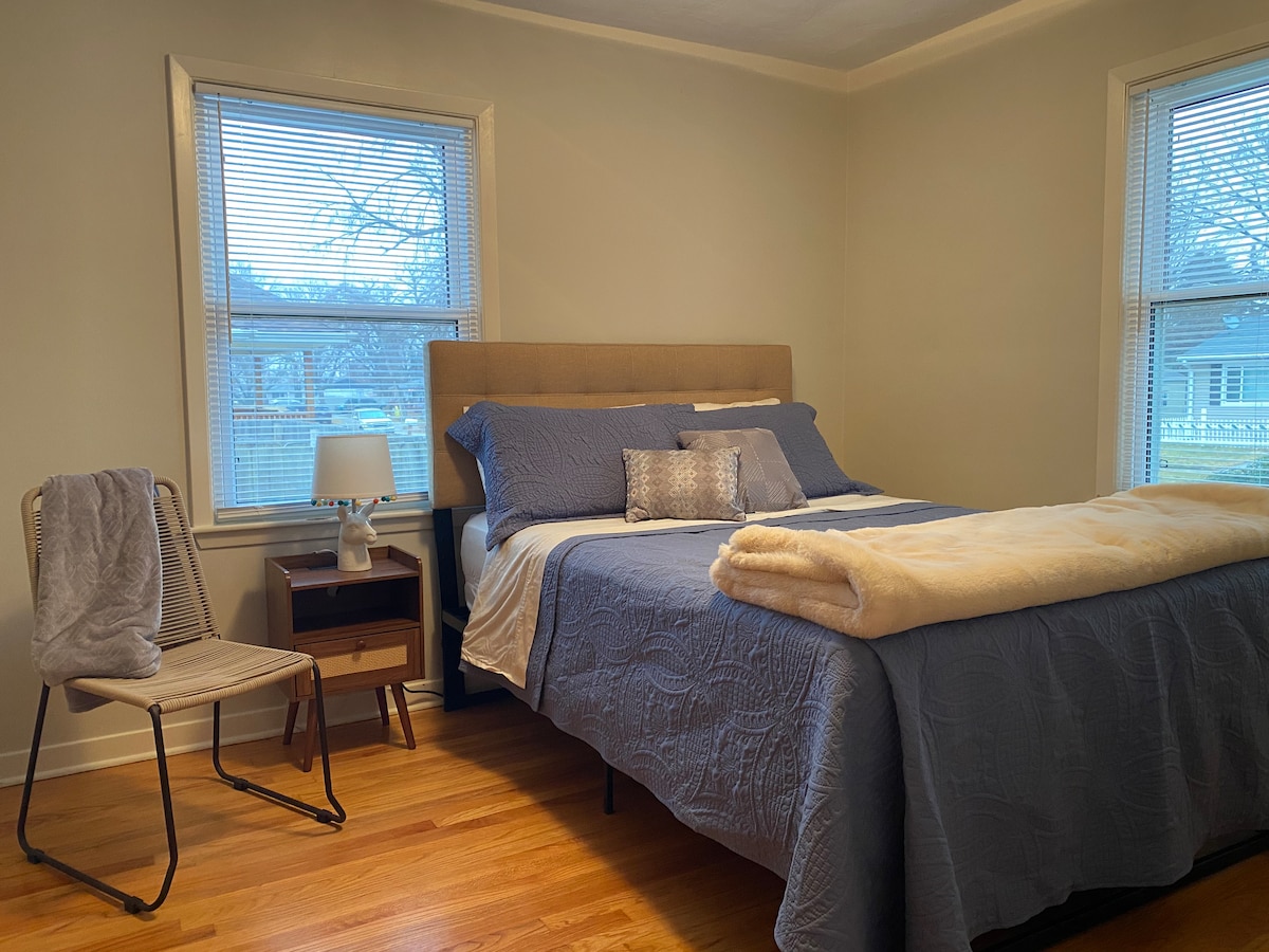 Slaapkamer 2: queensize bed met knus beddengoed, bedlamp en ochtendlicht. 