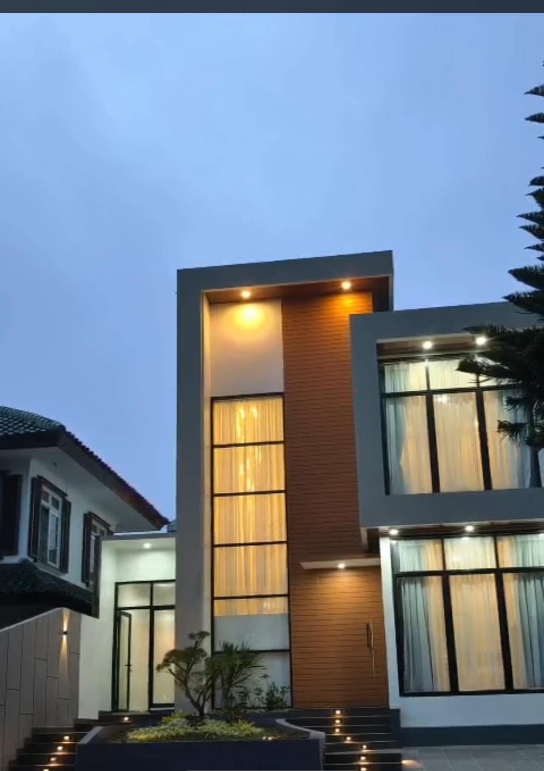 The modern villa exterior features a combination of sleek lines and warm lighting. Large glass windows allow natural light to fill the space, while decorative plants enhance the entrance. A contemporary architectural design is depicted, showcasing a two-tone color scheme with beige and brown elements.