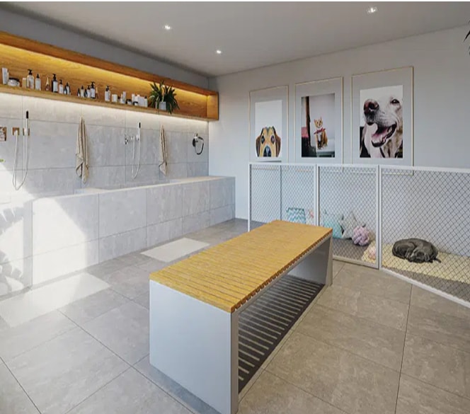 A well-lit room designed for pet care features a large bathing area with dual shower heads and storage for pet grooming supplies. A wooden bench serves as seating, while a cozy pet enclosure with a soft mat is positioned alongside framed pictures of dogs on the wall.