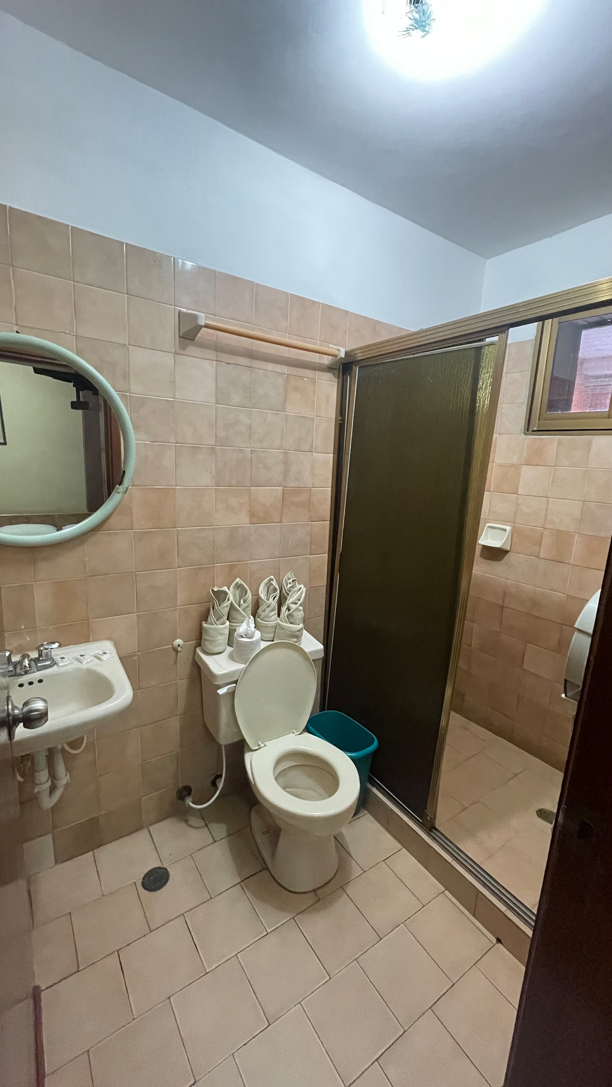 A compact bathroom is displayed, featuring beige tiled walls and floor. A shower area is enclosed with a glass door, while a toilet and a small sink are positioned thoughtfully. A round mirror hangs above the sink, adding function to the space.