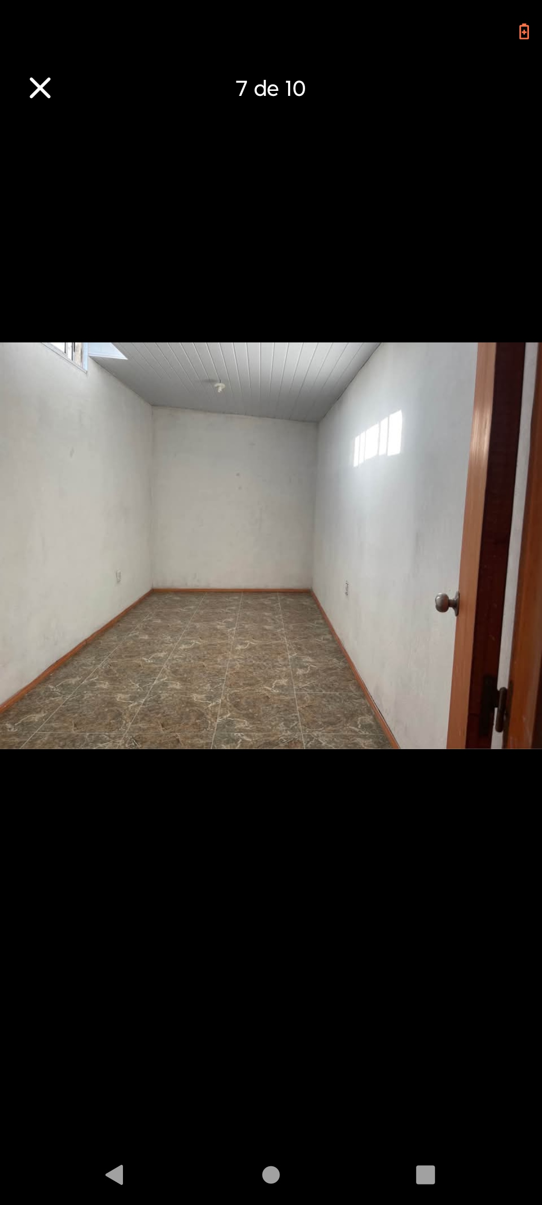 A shared room is presented with smooth light-colored walls and a simple ceiling. A small number of windows allows natural light to enter, illuminating the spacious floor area. The flooring features a patterned design, enhancing the room's overall versatility.