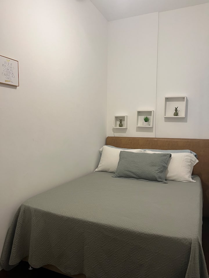 Quarto com cama de casal tamanho padrão, ar condicionado split e ventilador de teto.