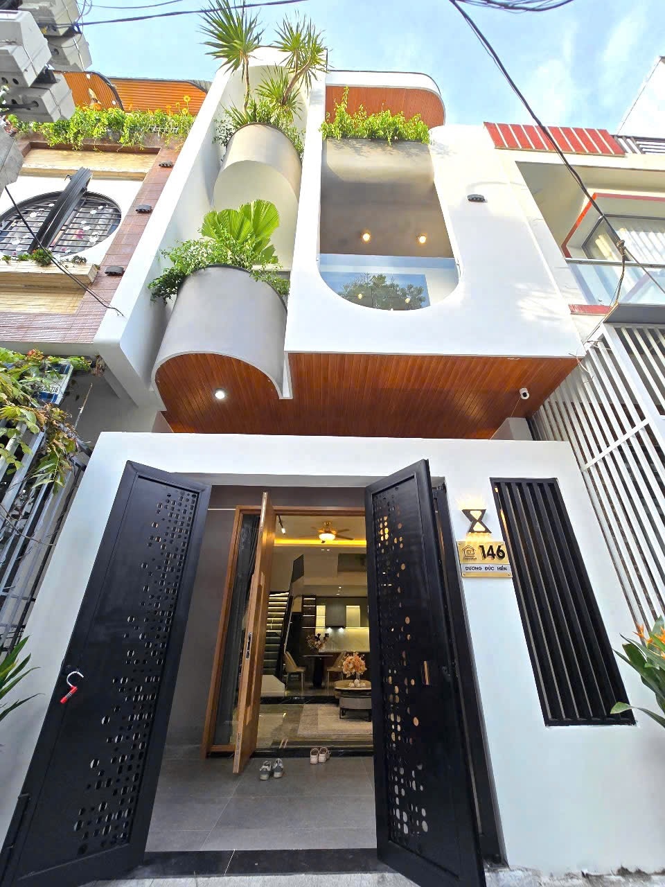 The entrance features an open doorway leading into the interior space. The exterior showcases a modern design with curved balconies adorned with greenery, harmonizing with a clean architectural style. Large windows contribute to a bright and welcoming appearance.