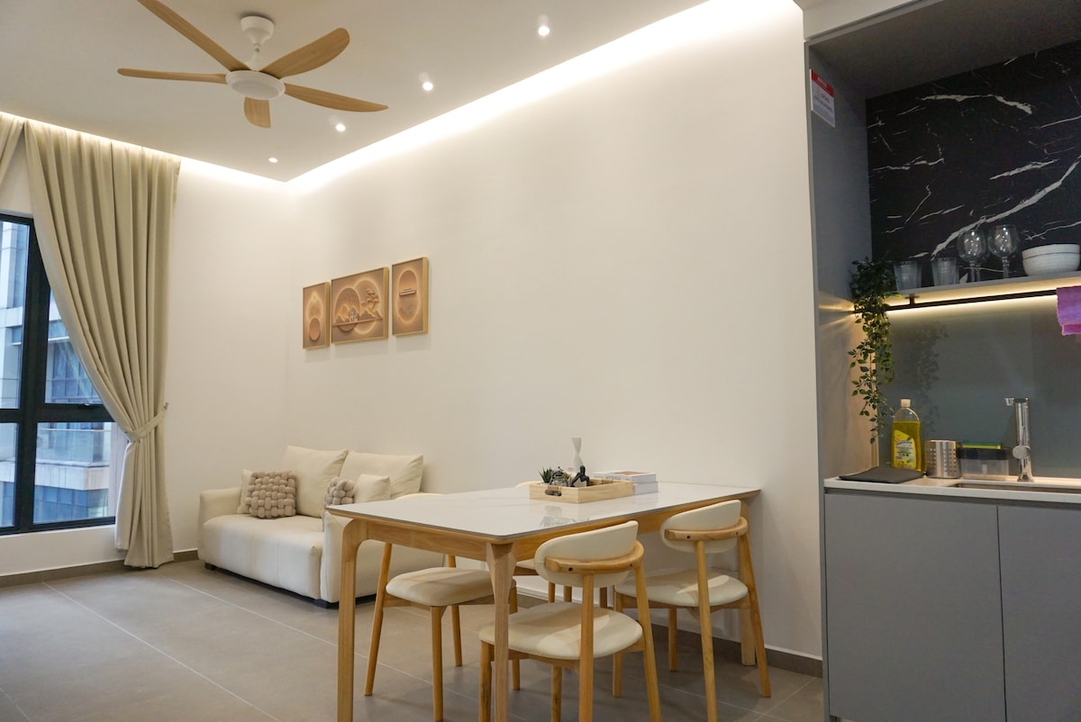 An airy living area is featured with a light color palette. A comfortable sofa is positioned beside a stylish table with wooden chairs. Natural light floods in through a large window, while elegant curtains frame the view.