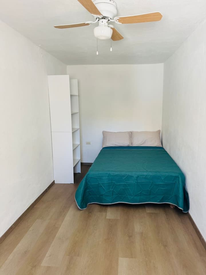 ห้องนอนพร้อมพัดลมเพดาน ตู้เสื้อผ้าขนาดเล็ก โต๊ะทำงาน และเตียงคู่