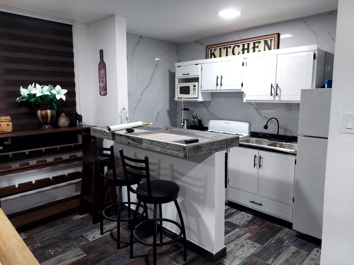 The kitchen area features white cabinetry and modern appliances, including a microwave and stove. A bar with high stools provides a casual dining space. A decorative kitchen sign is displayed on the wall, complemented by a small flower arrangement on the counter.
