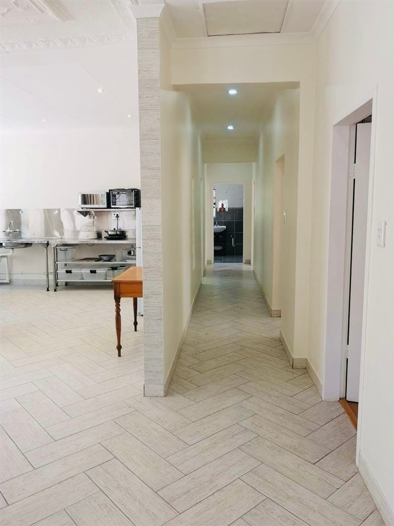 A well-lit hallway extends through the space, featuring pale, tiled flooring arranged in a herringbone pattern. Soft light fixtures illuminate the corridor, leading toward a kitchen area on the left and a bathroom visible at the end.