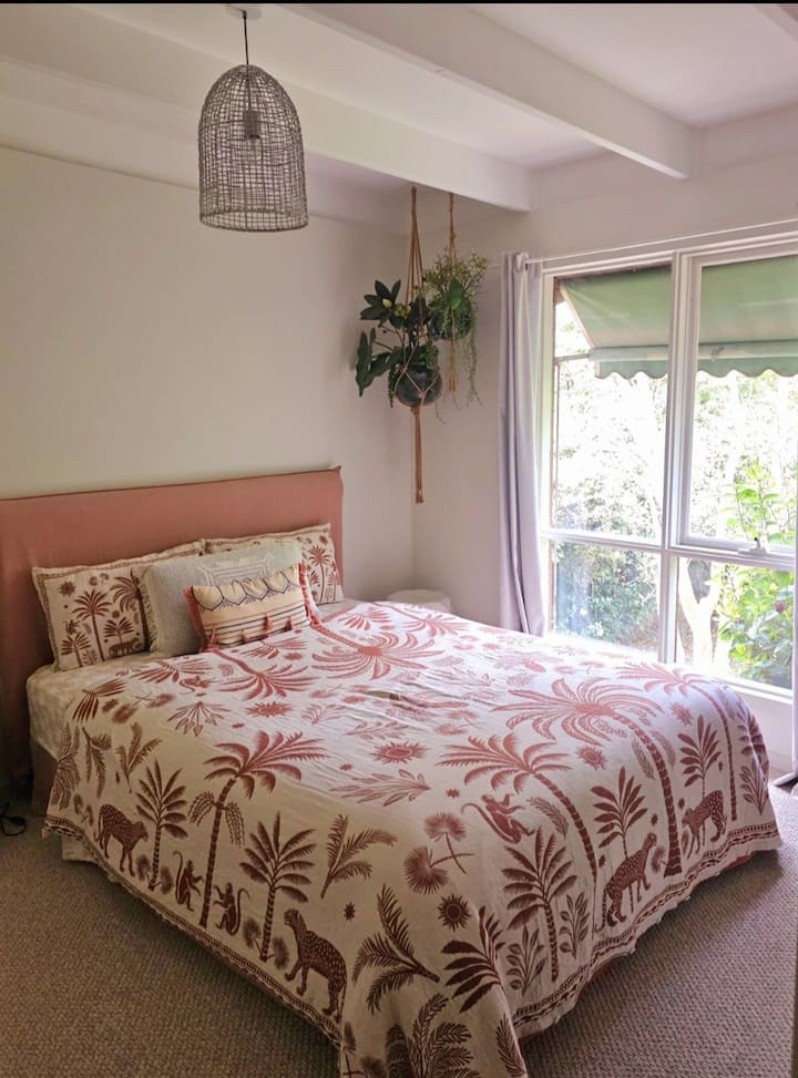 ห้องนอนที่อบอุ่นพร้อมเตียงควีนไซส์ ตะขอหลังประตูสำหรับแขวนเสื้อผ้าหรือผ้าเช็ดตัว และวิวสวยงามของสวน