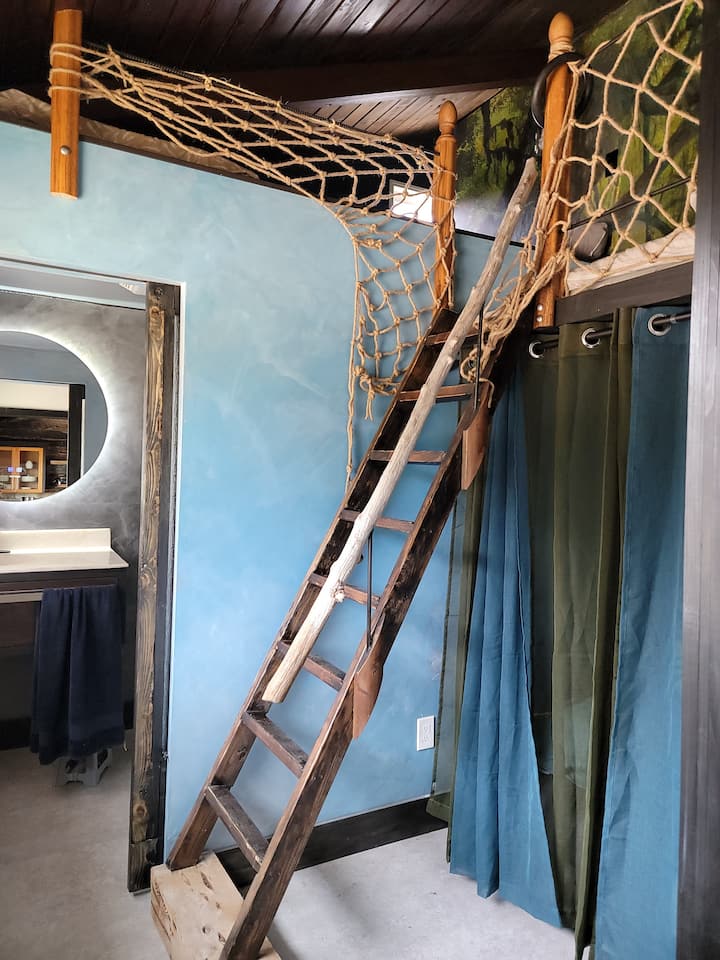 Tres niveles de literas para tres: una doble en una plataforma de >6' x 12', dos colchonetas japonesas con mantas (más cortas que las estándar), almohadas y mantas de felpa, una cortina opaca y una cortina de privacidad transparente.  