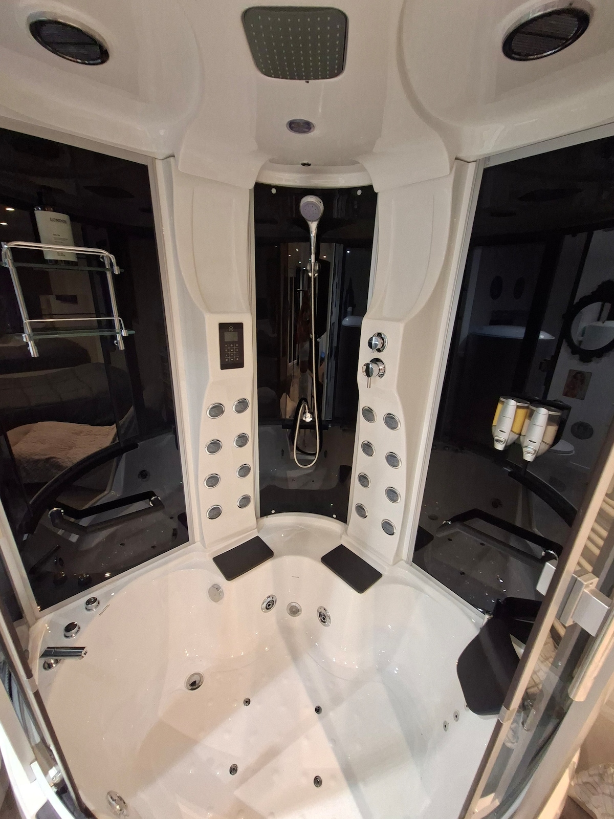 A modern shower and jacuzzi unit is presented, featuring multiple showerheads and numerous water jets. The sleek design includes a spacious seating area, elegant black panels, and neatly arranged toiletries. Suitable lighting enhances the overall appearance of this inviting wellness space.