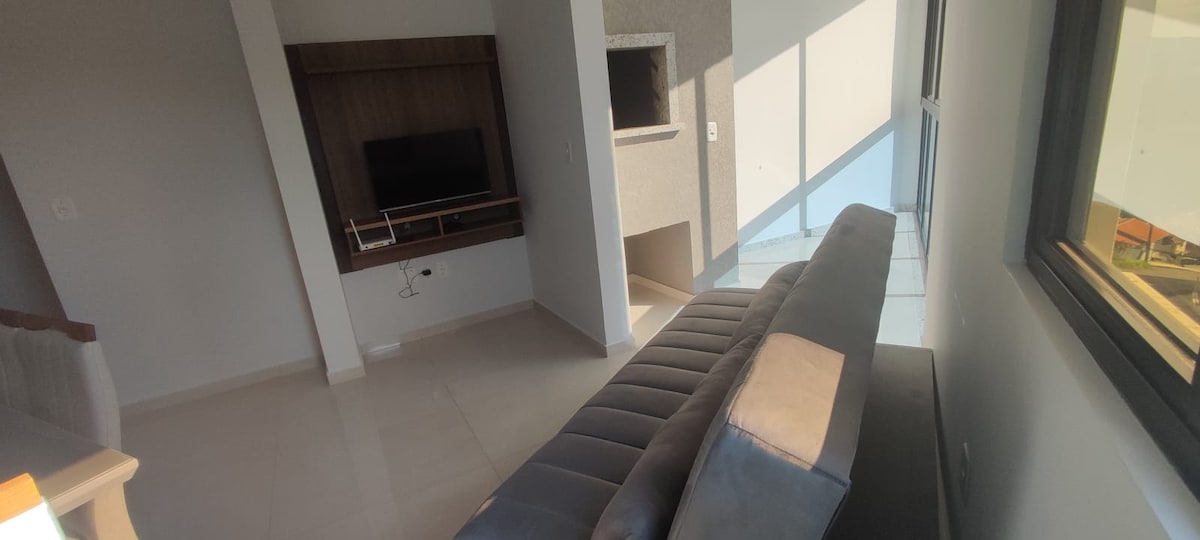 A spacious living area is captured, featuring a comfortable couch positioned near a large window that allows natural light to fill the space. A modern television is mounted on an accent wall, while a subtle fireplace is visible in the corner.