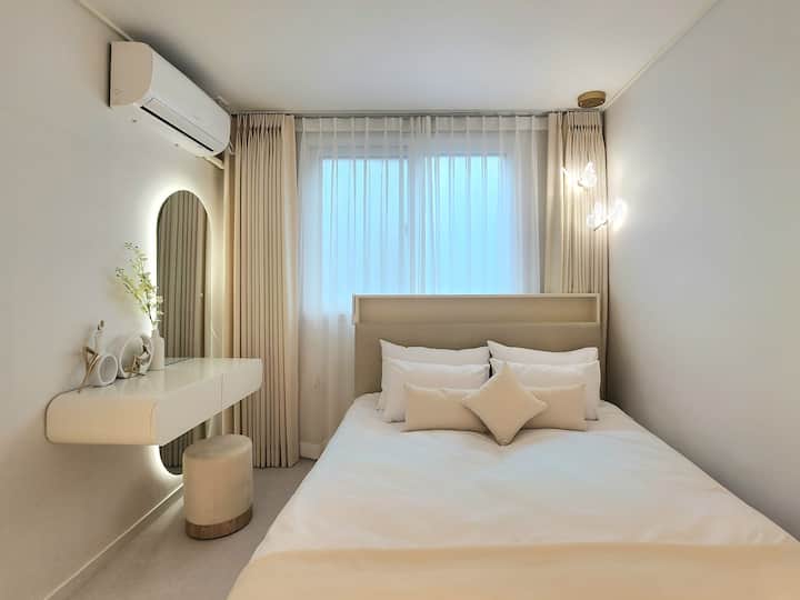 Завесите, теписите и перничињата во боја на слонова коска ја надополнуваат удобноста и стилското расположение на спалната соба 2 на Salu Stay.
Кога ќе ги повлечете завесите во боја на слонова коска, белата внатрешна завеса направена од шифон нежно ја филтрира сончевата светлина, создавајќи емоционална атмосфера, а истовремено ја зачувува приватноста.
Суптилното осветлување во форма на пеперутка станува препознатлив елемент, а предметите на шкафот за шминкање со LED осветлување се и функционални и чувствителни.