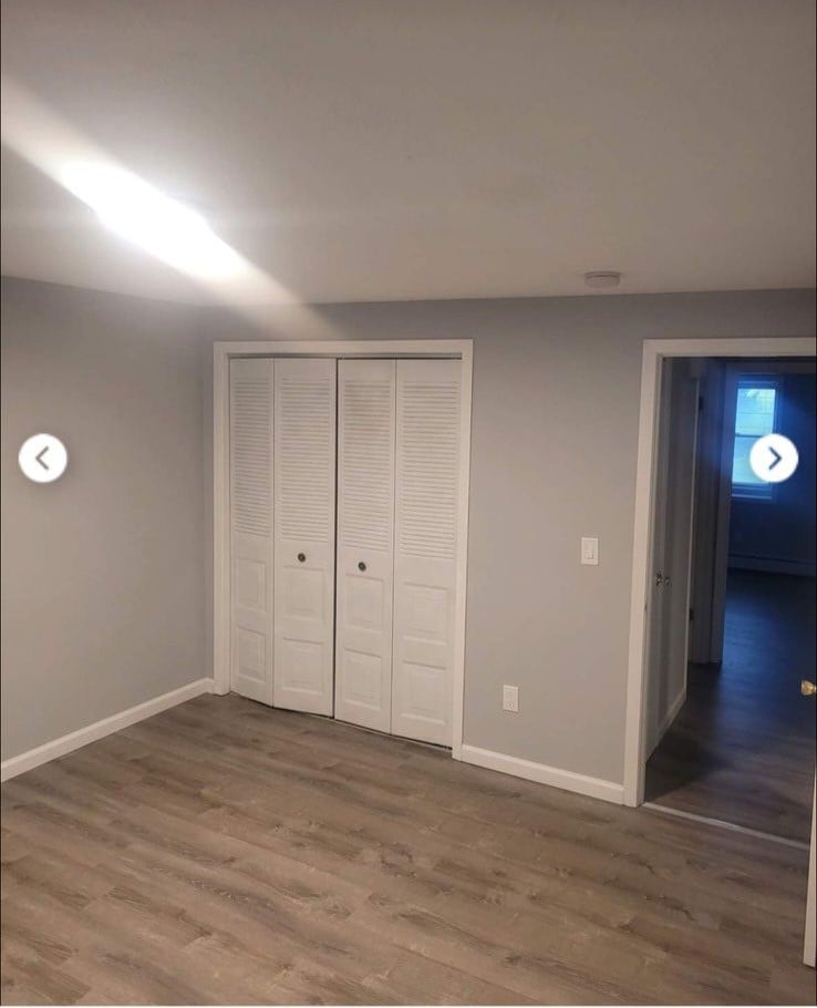A well-lit room features light gray walls and a laminate floor. Bi-fold closet doors are situated on one side, while a doorway leads to another room on the opposite side. Natural light is present, enhancing the spacious feel of the area.