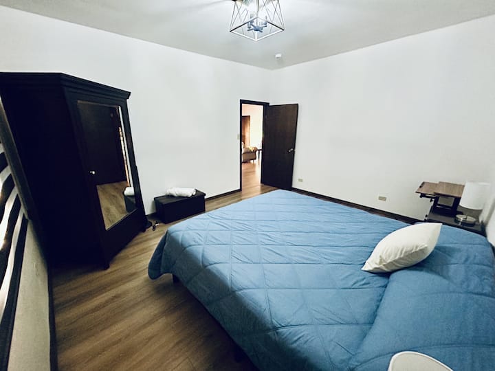 Spacious bedroom 1 with king-size bed, closet, dresser, nightstands, lamps, desk, portable fan, and blinds