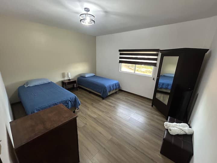 Spacious bedroom 2 with two twin beds, closet, nightstands, lamp, storage chest, and portable fan