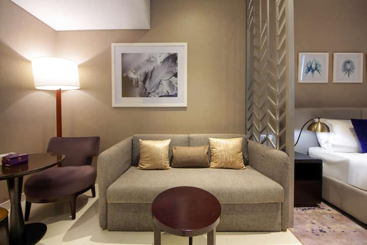 Bevind je in de woonkamer, waar een bank, zachte kussens en een bijzettafel een ontspannen plek creëren om te pauzeren tijdens je verblijf. De open indeling maakt het gemakkelijk om door de ruimte te bewegen, waardoor je een comfortabele plek hebt om tot rust te komen in Dubai.