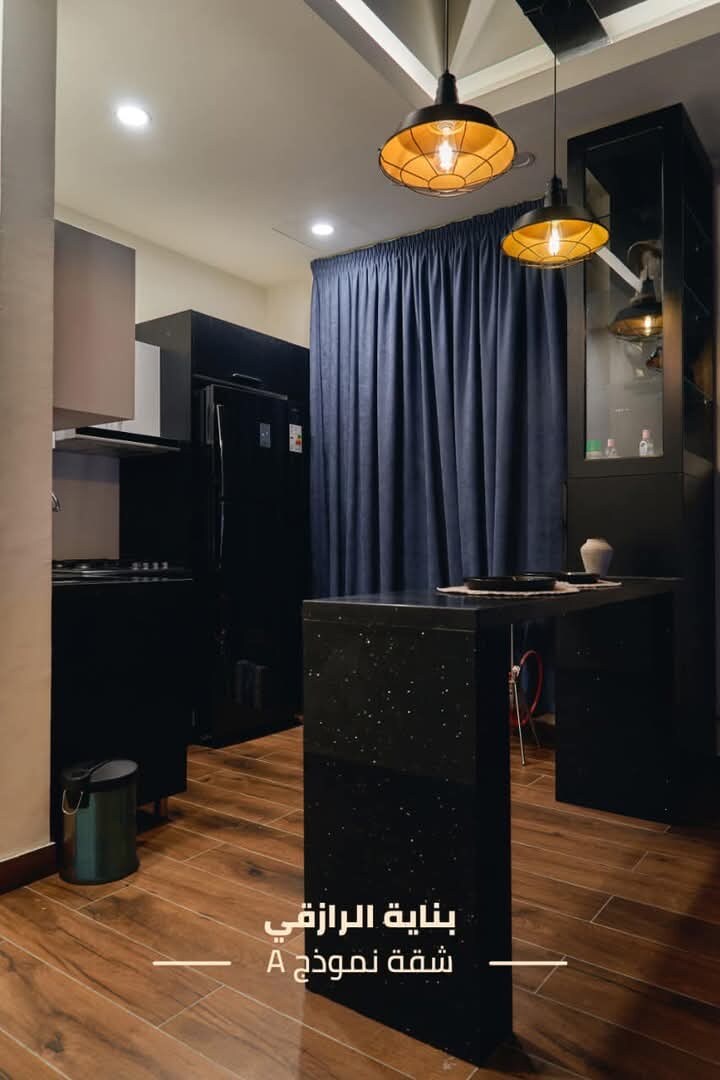 A modern kitchen space is highlighted, featuring dark cabinetry and a contrasting countertop. Pendant lights provide soft illumination above a small dining area. A dark curtain is drawn, adding a touch of privacy.
