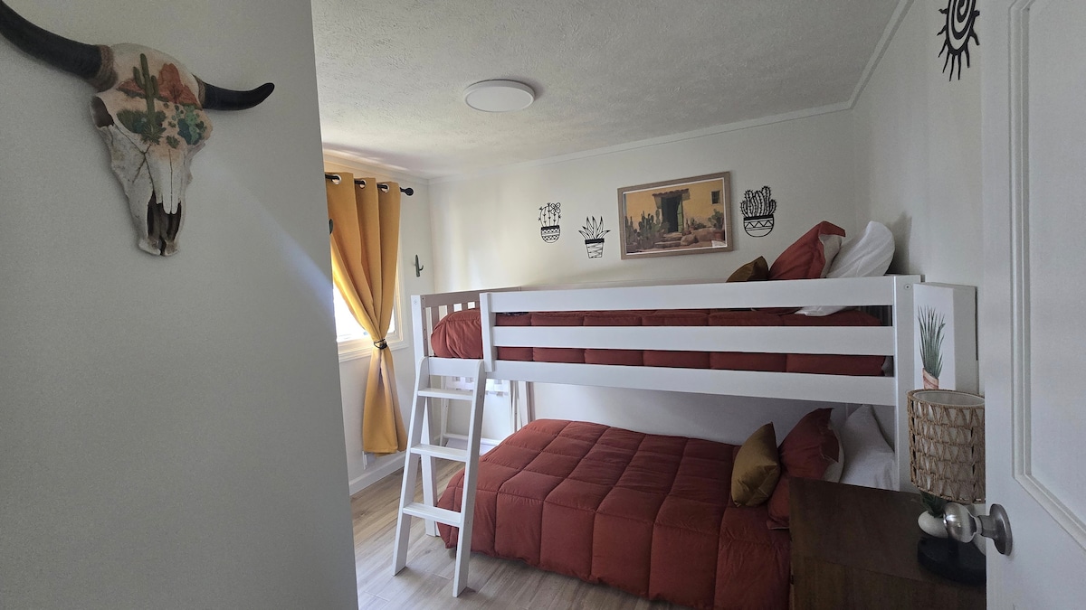 Dit is onze Aztec-geïnspireerde slaapkamer. Het is karakteristiek, met woestijnkunst, metalen cactusaccenten en een warm zonnemotief. Mosterd verduisterende gordijnen en gebrand oranje beddengoed creëren een gedurfde maar gezellige retraite voor een goede nachtrust. Twin stapelbedden  