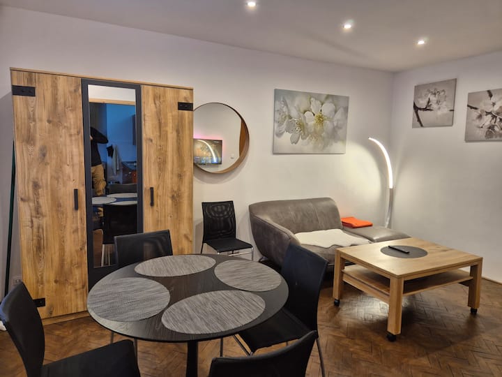 Spazio abitativo luminoso ed elegantemente arredato con zona pranzo, comodo divano e illuminazione moderna: un luogo ideale per trascorrere del tempo insieme, rilassarsi e riunirsi la sera.