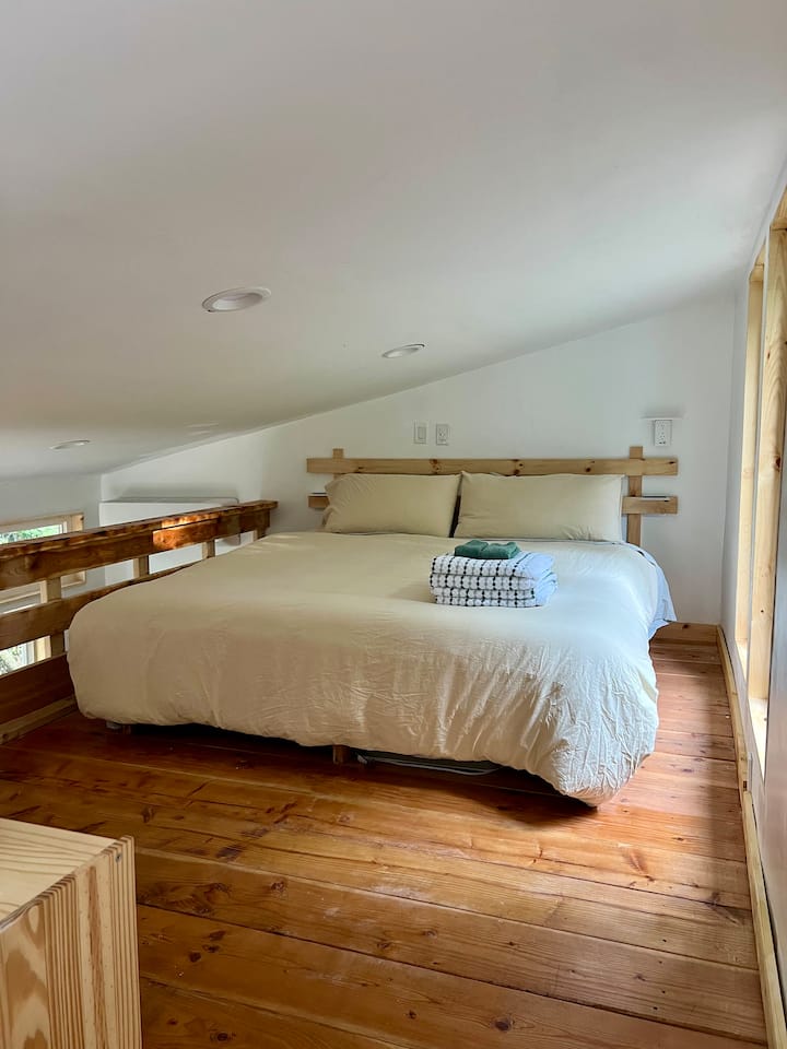 Spavaća soba u potkrovlju s bračnim krevetom. Stolni ventilator ispod kreveta za bijelu buku ili dodatnu cirkulaciju zraka