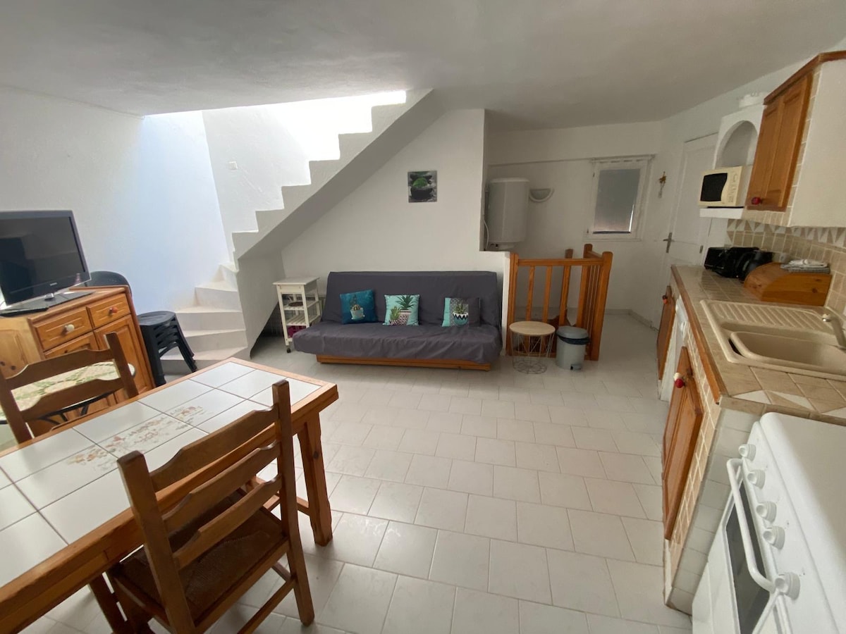 An open living space is observed, featuring a comfortable sofa, a wooden dining table with chairs, and a television. Light floods in through a skylight above a staircase. The kitchen area includes essential appliances and cabinetry, contributing to a warm and functional atmosphere.