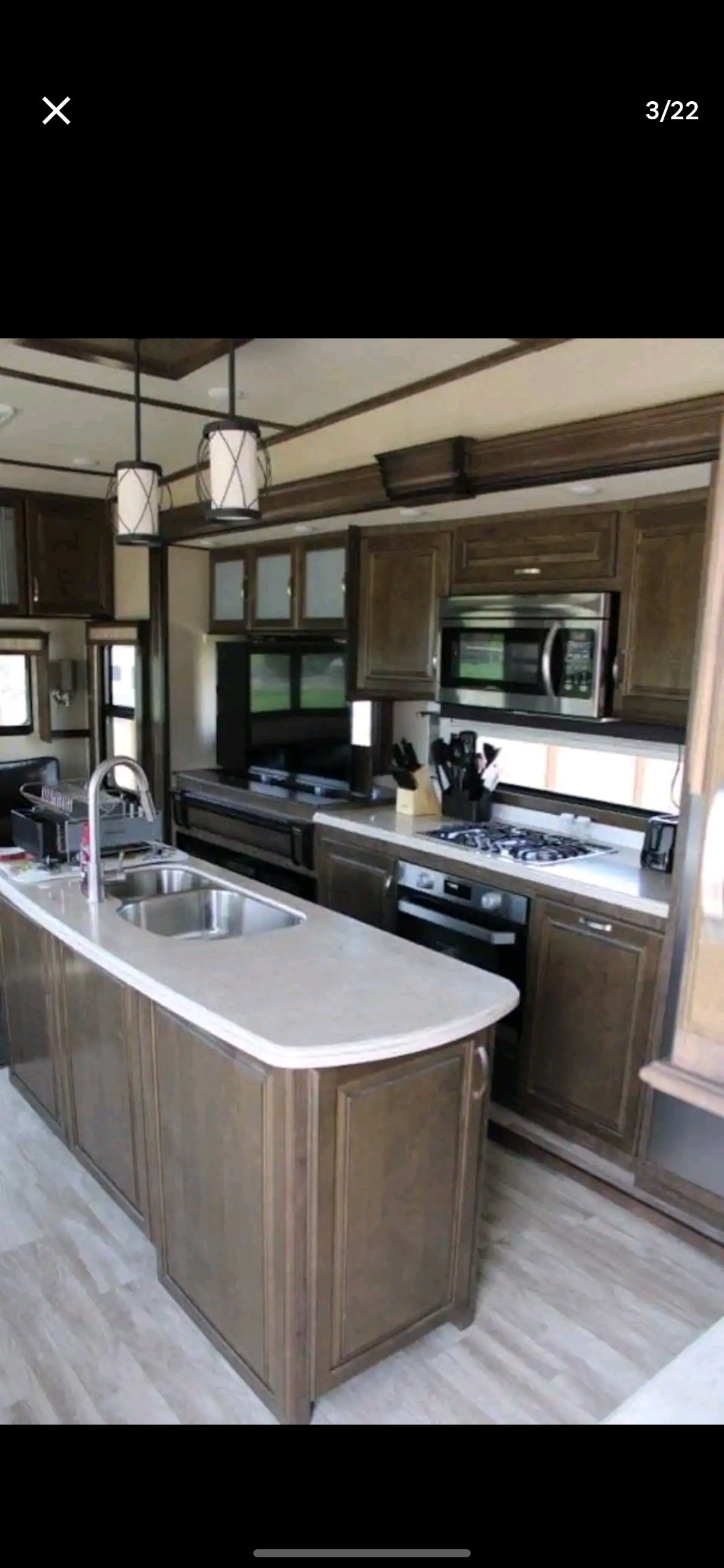 A well-equipped kitchen features wooden cabinetry and stainless steel appliances, including a microwave and a stove. A central island with a smooth countertop is complemented by a double sink. Natural light is provided through windows, enhancing the space's functionality.