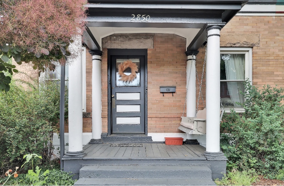 The entrance features a classic porch with white columns supporting a shaded roof. A decorative wreath adorns the front door, which is flanked by windows. Lush greenery surrounds the entrance, creating a welcoming approach to the home.