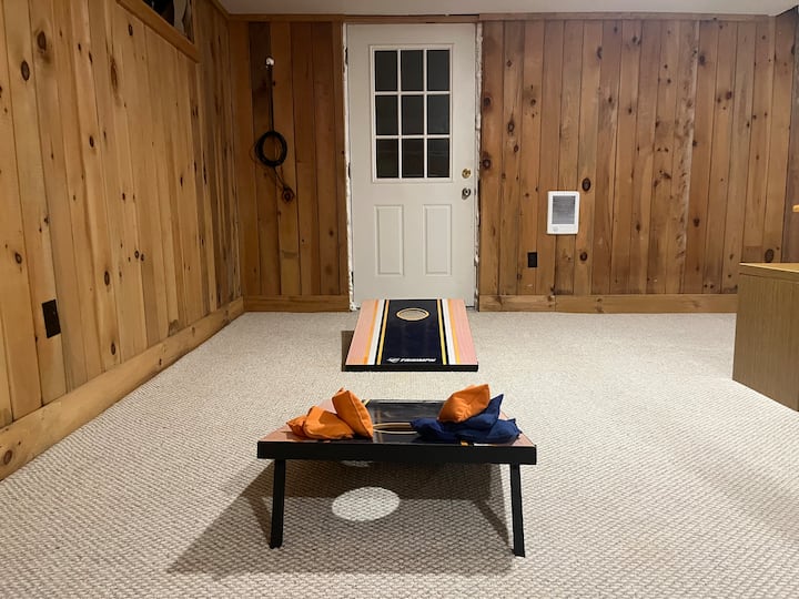 בחדר השינה/חדר המשחקים במרתף יש תנור פרופן, טלוויזיה חכמה 55 אינץ', משחק קורנ הול, 2 פופים, שולחן משחקים/פאזל ומזרן מתנפח יחיד. 