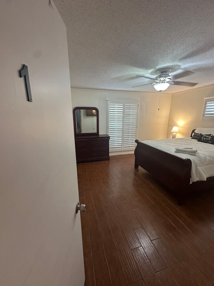 ห้องนอนใหญ่พร้อมห้องน้ำส่วนตัว เตียงควีนไซส์ ตู้ลิ้นชักพร้อมกระจก โต๊ะข้างเตียง โคมไฟ สายต่อพร้อมเต้ารับ 8 ช่อง พอร์ต USB และ USB-C สมาร์ททีวีขนาด 55” และกระจกบานประตูแบบเต็มตัว