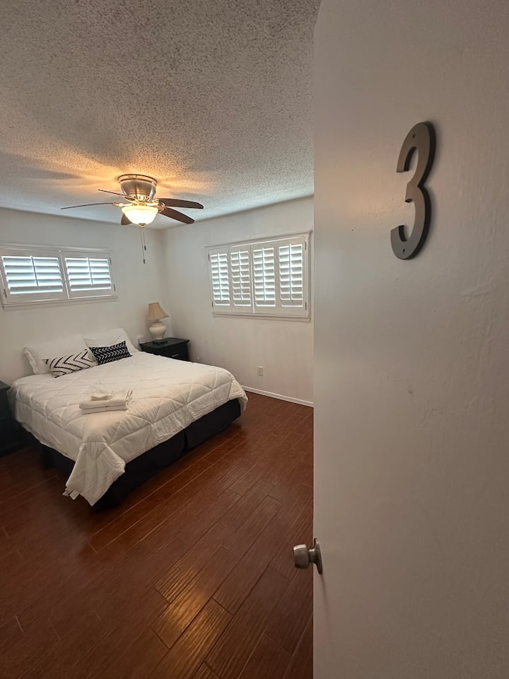 เตียงควีนไซส์ โต๊ะข้างเตียง 2 ตัว แต่ละตัวมีโคมไฟ สายไฟต่อ 2 สายพร้อมเต้ารับ 8 ตัว พอร์ต USB และ USB-C และกระจกส่องตัวเต็มตัว