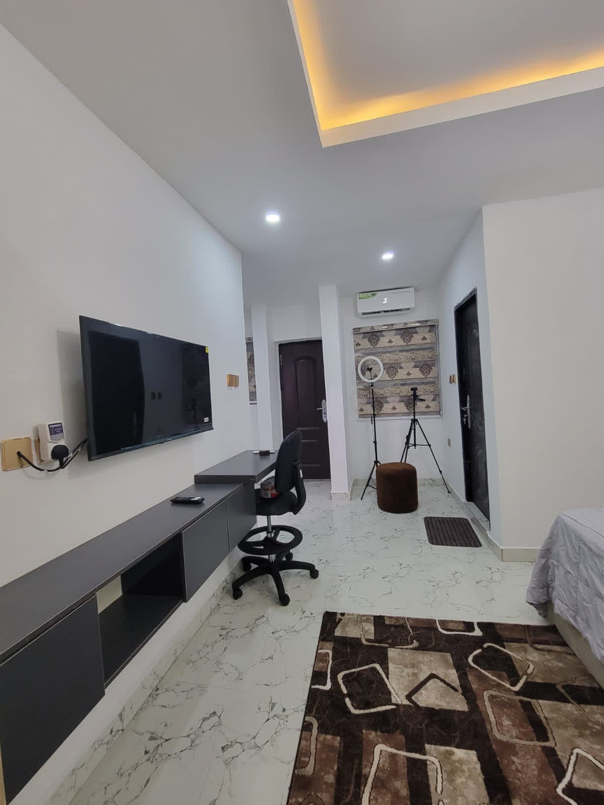 A modern bedroom space is highlighted, featuring a plush bed and a 32" Smart TV mounted on the wall. A work desk and chair are positioned in front of the TV. The room is adorned with a patterned rug, and soft lighting adds a calming touch.