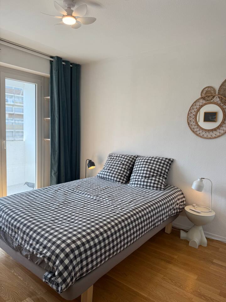 Spálňa s rozlohou 12 m², manželská posteľ s rozmermi 140 x 200 cm, priestranná šatňa, kreslo, stropný ventilátor a veľké sklenené okno s výhľadom na balkón.