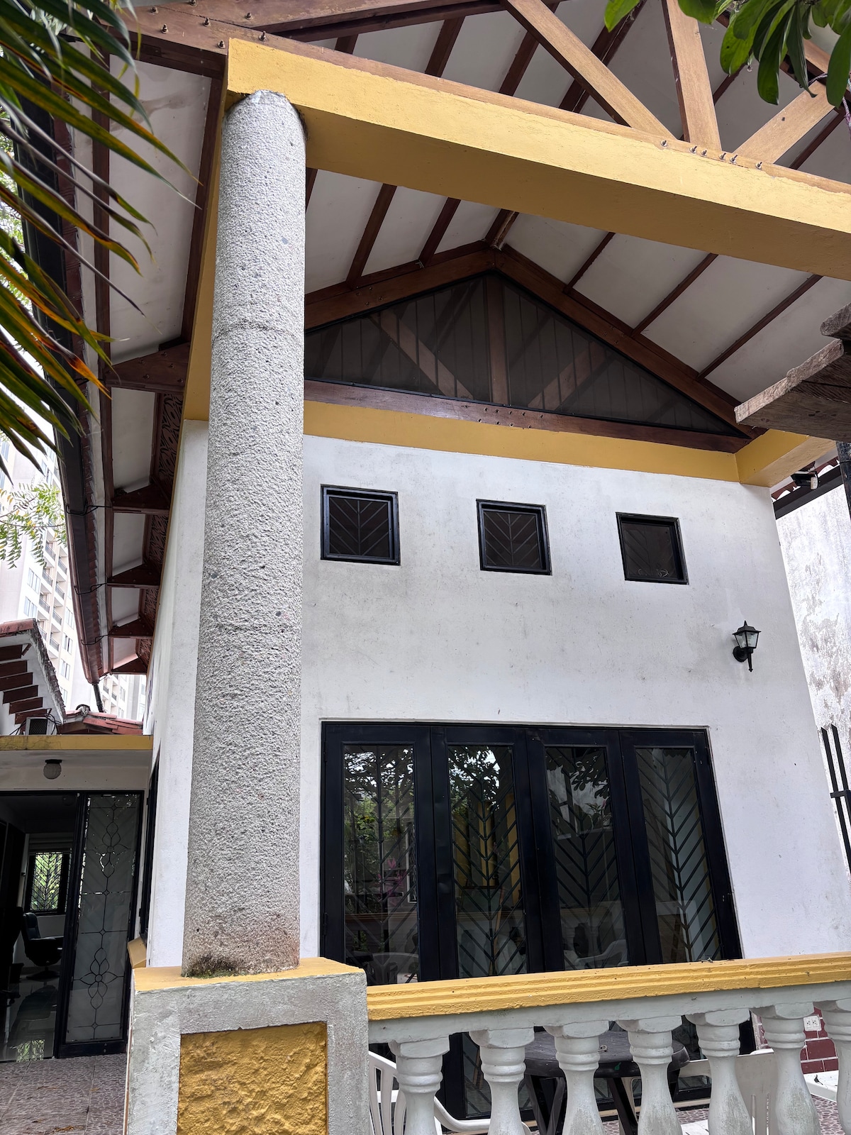 The exterior of the house features a striking triangular roof with a wooden framework. Large glass doors are visible, allowing natural light to illuminate the interior. The façade is complemented by distinctive windows and a decorative railing, enhancing the home's inviting character.