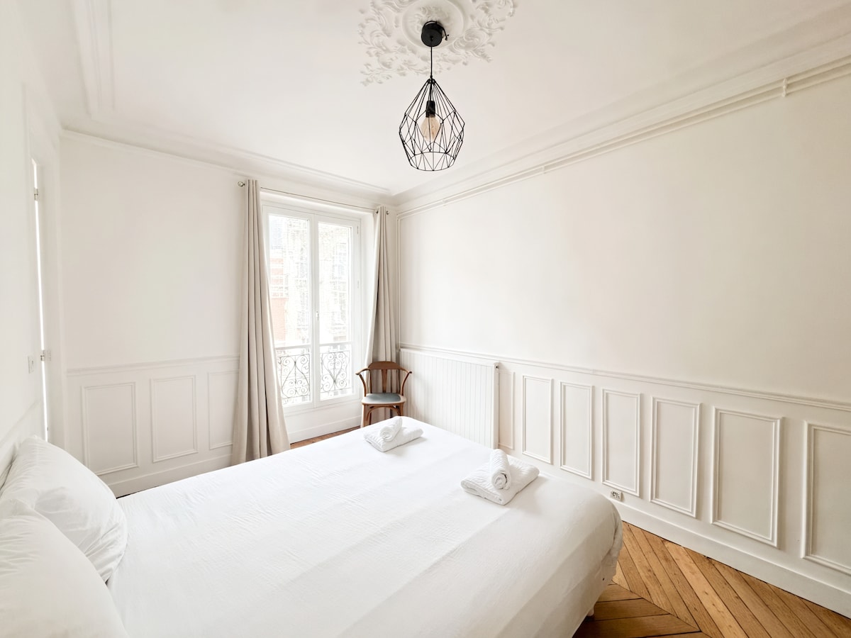 Última vista de la habitación, destacando su ambiente luminoso y su mobiliario depurado. El suelo de madera y las paredes blancas crean un ambiente relajante, ideal para un sueño reparador.