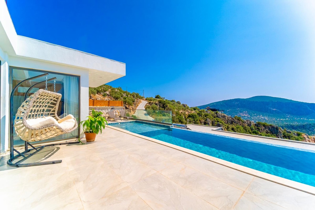 An outdoor terrace features a spacious swimming pool surrounded by tiled flooring. A hanging chair is positioned nearby, complemented by a potted plant. The background showcases rolling hills and a clear sky, offering an unobstructed view of the landscape.