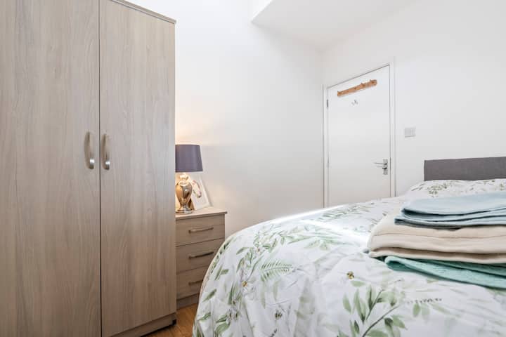 „Svijetla spavaća soba s bračnim krevetom, svježom posteljinom, ormarom i noćnim ormarićem s lampom.”