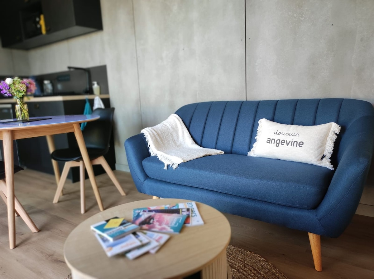 A modern seating area features a blue couch with decorative throw pillows, complemented by a round coffee table. A dining table with wooden legs and a black chair is positioned nearby. Fresh flowers are arranged in a vase, adding a touch of color to the space.